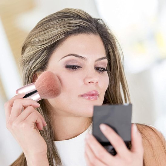 Femme tenant un pinceau maquillage en se  regardant dans le miroir